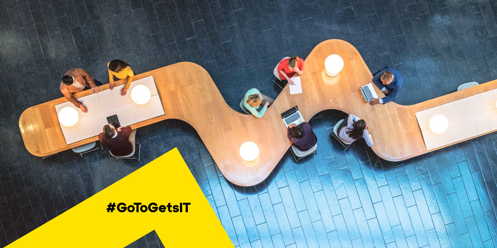 Overhead view of a communal flex workspace where SMB co-workers are collaborating on laptops and mobile devices, highlighting the need for remote IT management and support by MSPs