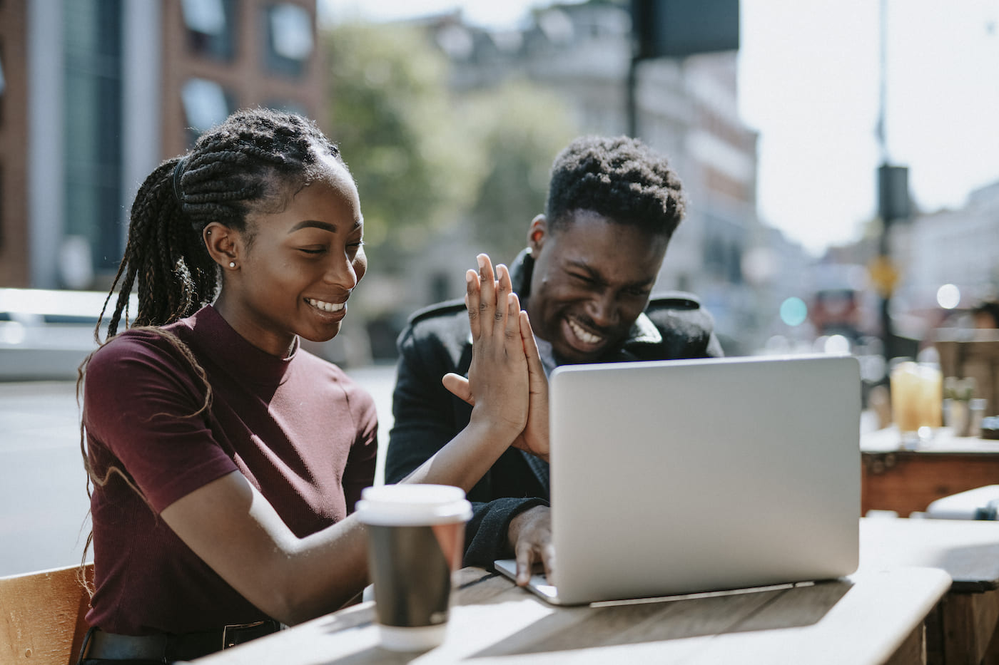 Young man and woman working outside at a street cafe high-fiving over a laptop